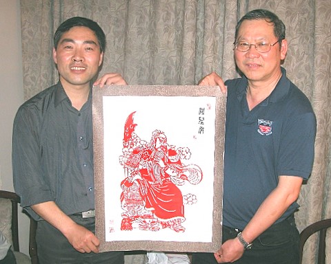 2006年5月，关健中先生(右)带头捐助关公网，关公网回赠剪纸作品表示感谢 